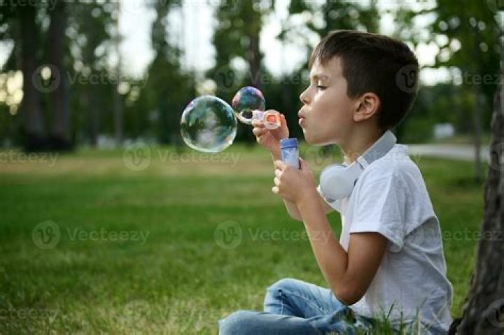 A boy blowing bubbles at bat in blue. 